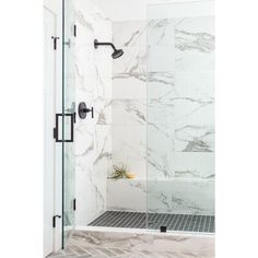 a bathroom with white marble walls and flooring, shower head, and glass door