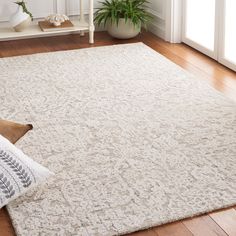 a large white rug in the middle of a room with wooden flooring and potted plants