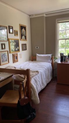 a bed sitting in a bedroom next to a wooden desk and window with pictures on the wall