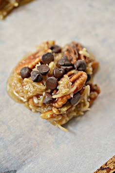 a cookie with chocolate chips and pecans on top sitting on a piece of parchment paper