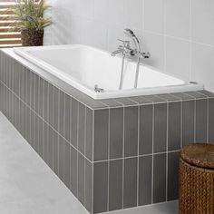 a bath tub sitting next to a wooden stool in a white tiled bathroom with grey tiles on the walls