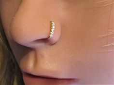 a woman's nose with a gold nose ring on top of her nose and two small white pearls in the middle