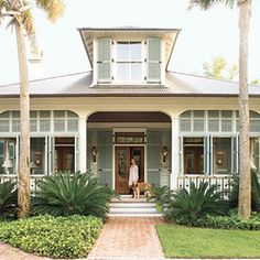 a house with palm trees in front of it and a woman standing on the porch