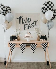 a table topped with cake and balloons in front of a sign that says two fast