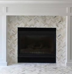 a white fireplace with a black mantle and marble tile on the top part of it