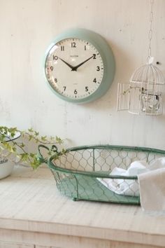 a clock on the wall above a wire basket with towels and plants in it next to a birdcage