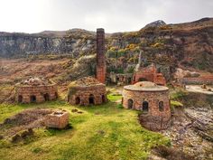 an old stone building in the middle of a grassy area next to a mountain range