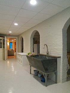 a kitchen with white walls and flooring has a large sink in the center, along with an arched doorway leading to another room