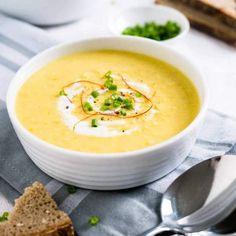 there is a bowl of soup on the table with bread and green garnish