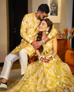 a man and woman sitting on top of each other in front of a couch wearing yellow dresses