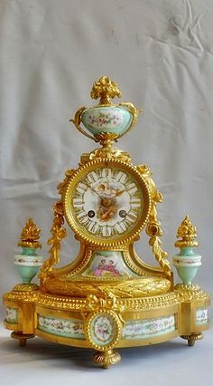 an ornate gold clock with green and white decorations on it's sides, against a plain background