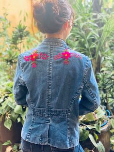 the back of a woman's jean jacket with flowers embroidered on it and in front of potted plants