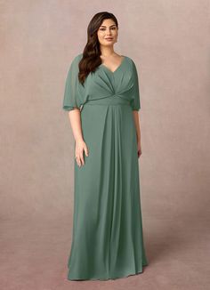 a woman in a long green dress standing on a gray background with her hands behind her back