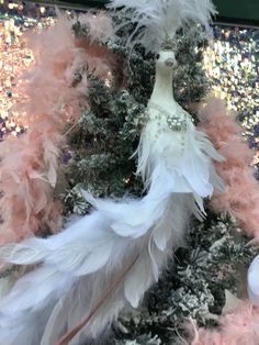 a white and pink christmas tree with feathers on it's top, surrounded by glitter