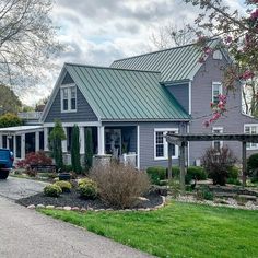 a blue truck is parked in front of a gray house with a green metal roof