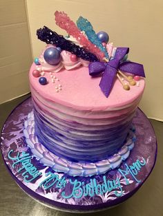 a birthday cake decorated with pink and blue frosting, purple icing and decorations