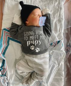 a baby is sleeping with a pacifier in it's mouth and wearing a shirt that says going home to meet my pups