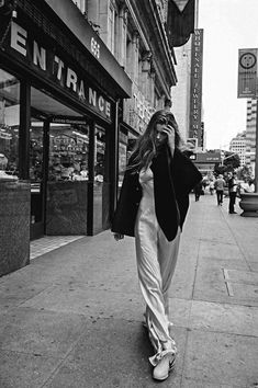 a woman is walking down the sidewalk talking on her cell phone while wearing all white