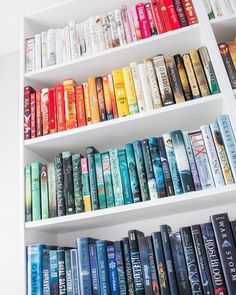 a book shelf filled with lots of books on top of white shelves next to a wall