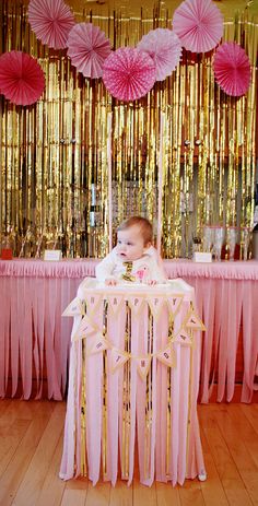 a baby is sitting at a table with pink and gold decorations