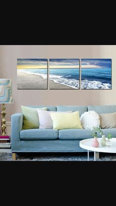 three paintings on the wall of a living room with a couch and coffee table in front of it