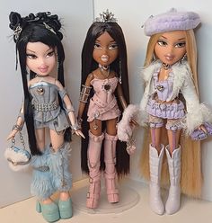 three dolls standing next to each other in front of a wall with white walls behind them