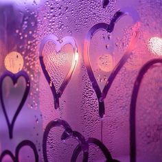 three hearts drawn on a window with water droplets and lights in the backround