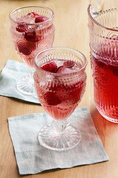 two glasses filled with raspberry punch on top of a wooden table next to napkins