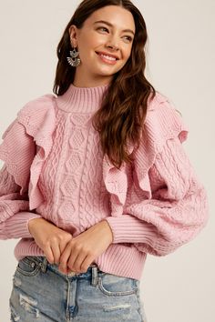 a woman wearing a pink sweater with ruffles on the sleeves and bottom, smiling