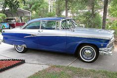 an old blue and silver car parked in front of a house next to some trees