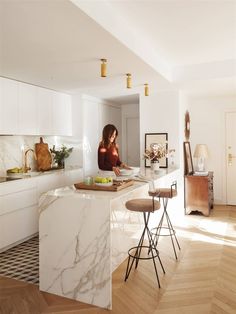 a woman standing at the kitchen counter in front of an island with two stools