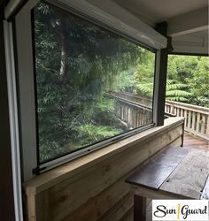 an open window on the side of a wooden deck overlooking a lush green forest filled with trees