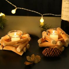 two candles sitting on top of wooden logs next to a bottle of wine and pine cones