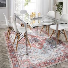 a glass dining table with white chairs and a red rug in front of the window