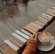 a cup of coffee sitting on top of a wooden table next to stacks of books