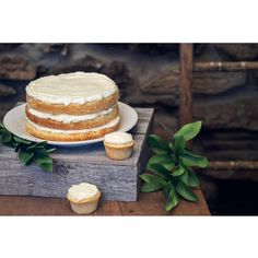 a cake sitting on top of a wooden table next to cupcakes and greenery