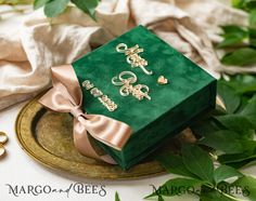 a green box with two initials on it sitting on a plate next to greenery