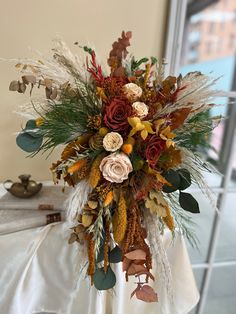 a vase filled with flowers and leaves on top of a white tablecloth covered table