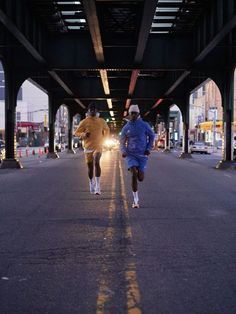 two men running under an overpass in the city at night, one is wearing a blue jacket