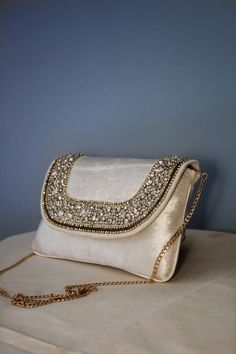 Presenting exquisite clutch with detachable shoulder sling. The classy clutch for wedding day is embellished with beautiful rhinestones, with a tad of classy elegant 'zardosi work' (a form of embroidery done through metallic threads). This white clutch is very unique and will go with every function. Be it wedding or any party. Discover exquisite elegance with our handcrafted velvet clutch, a perfect bridal accessory for your wedding day. This rhinestone-studded women's clutch exudes minimalist charm, complementing your bridal ensemble. Designed for the ethereal bride, this ethnic clutch seamlessly fuses tradition and modernity. Explore our collection of ladies purses, and find the ideal rhinestone handbag to enhance your wedding style. Luxury White Evening Bag For Wedding Guest, Luxury Stone Embellished Wedding Bags, Elegant Hand Embellished Clutch Shoulder Bag, Glamorous White Embellished Clutch, Elegant Hand-embellished Wedding Bag, Luxury Hand Embellished Shoulder Bag For Wedding, Elegant Hand Embellished Clutch Evening Bag, Embellished White Clutch Evening Bag, Luxury Wedding Shoulder Bag With Pearl Embroidery