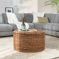 a wicker coffee table in the middle of a living room with grey couches