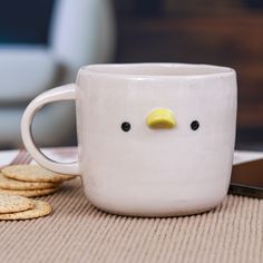 a white mug with a yellow beak sitting on top of a table next to crackers