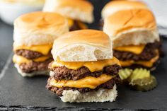 three cheeseburger sliders with pickles on a slate board, ready to be eaten