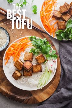 two plates filled with tofu, carrots and rice on top of a wooden cutting board