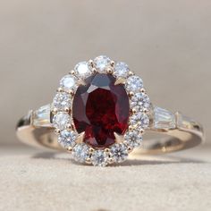 a close up of a ring with a red and white stone in the center, surrounded by diamonds