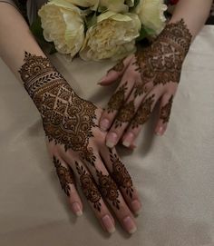 two hands with henna designs on them next to some white flowers and a bouquet