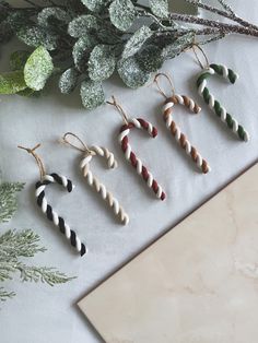 four christmas ornaments hanging from strings on a table next to greenery and a cutting board