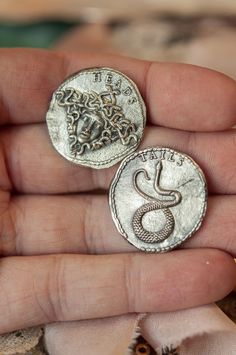 a person is holding two silver coins in their hand and the other one has a snake on it