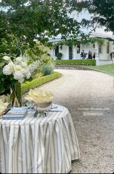 there is a table with flowers on it in front of a large white house and trees