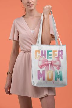 Elevate your game day essentials with our "Cheer Mom" 📣 Canvas Tote Bag! Perfect for proud cheerleader moms, this durable, eco-friendly tote showcases a vibrant, large pink bow 🎀 and colorful letters "Cheer Mom" print on both sides, embodying the spirit of cheerleading with style and convenience. Crafted to carry all your necessities, from pom-poms to snacks, its spacious interior and sturdy handles make it your go-to bag for every cheer event and beyond.  Available in 3 sizes to add both functionality and style, these custom-printed tote bags come with multiple handle colors to match your designs. Made with spun polyester, these bags feature double-stitched seams, cotton webbing straps, and nonwoven laminate lining for high-end durability.  .: Made with 100% polyester, a medium-weight f Casual Shoulder Bag For Mother's Day, White Canvas Bag For School, Retro White Bags With Letter Print, Retro White Bag With Letter Print, White Canvas Shoulder Bag For Mother's Day, Fun White Letter Print Bag, White Shoulder Bag With Letter Print For Mother's Day, Cheer Competition, Cheerleading Mom